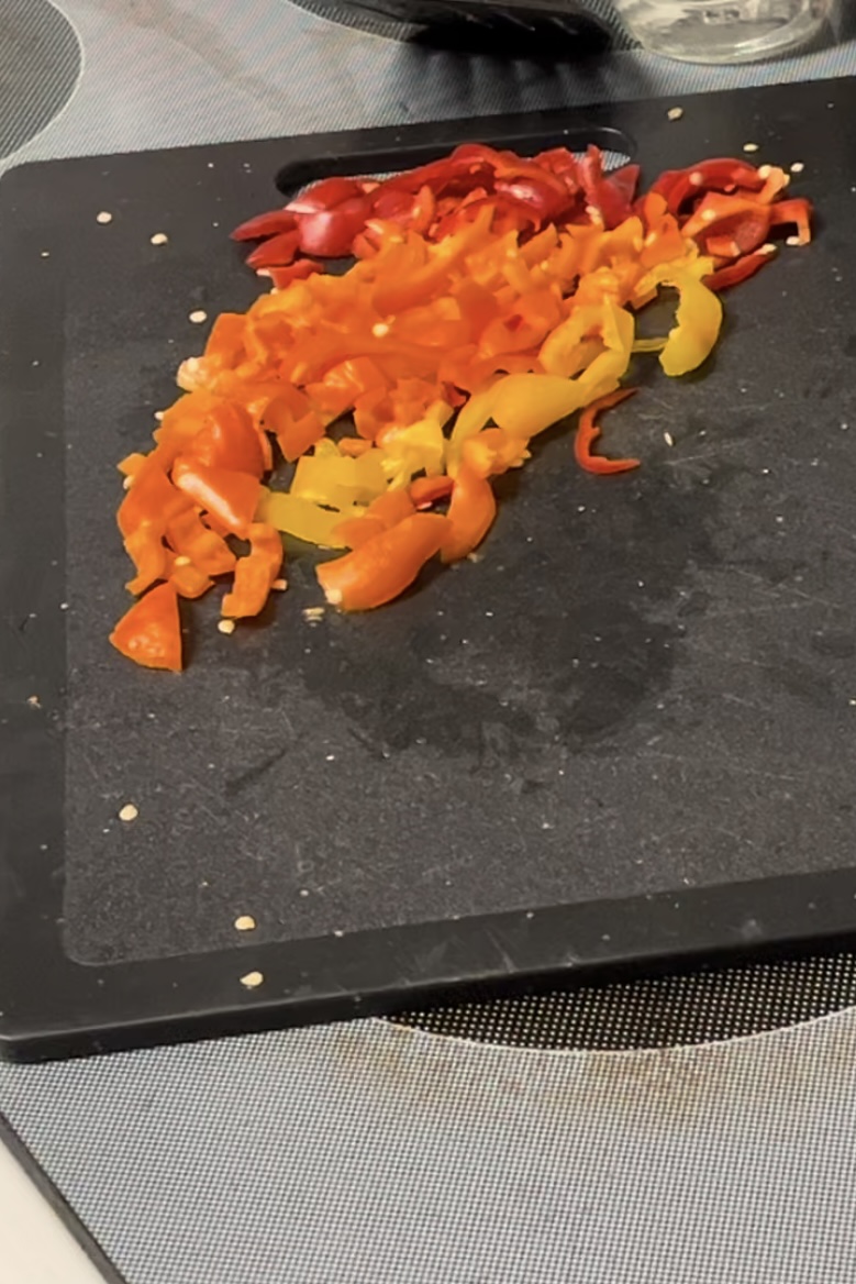 Red yellow and orange bell peppers all cut up siting on a black cutting board