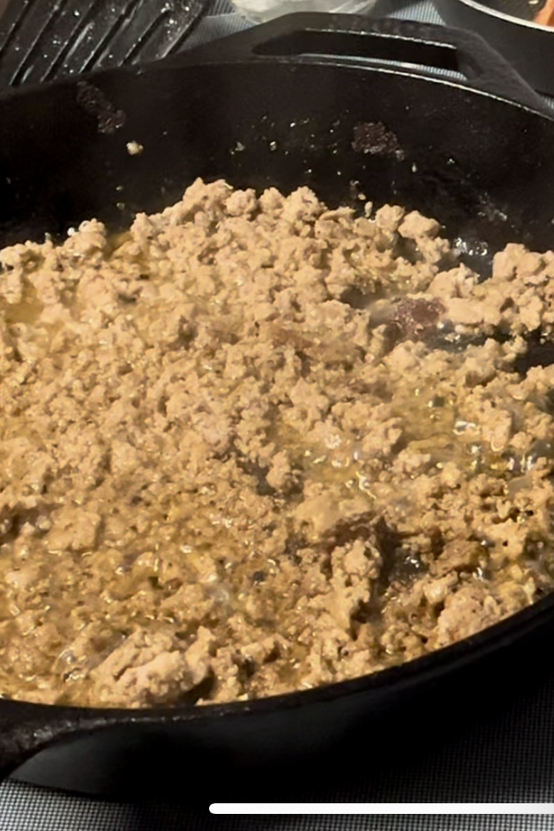 Meet has been broken up and is being cooked in a cast iron pan