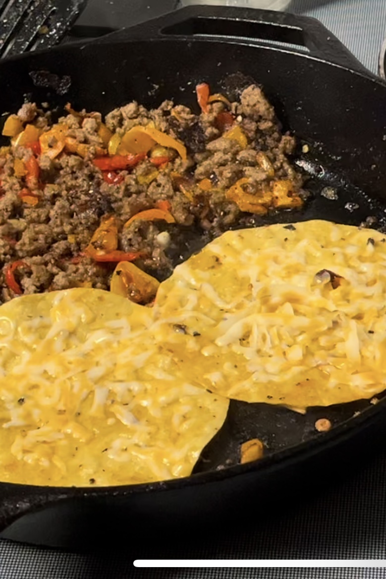Meat has been cooked and pushed to side with peppers. Two tortillas have been added and have cheese on them that has stared to melt