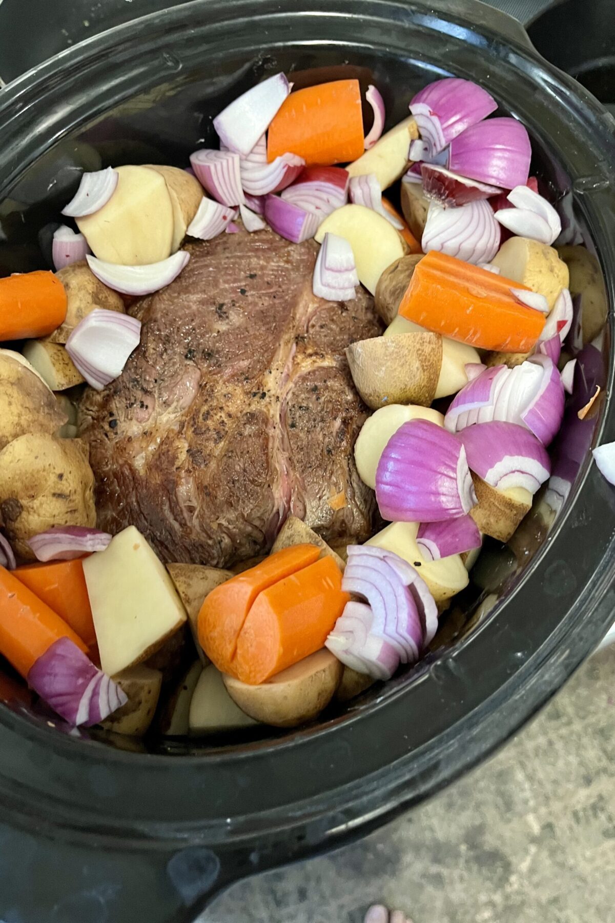 Roast has been added to crockpot and has had onions, carrots and potatoes added around it