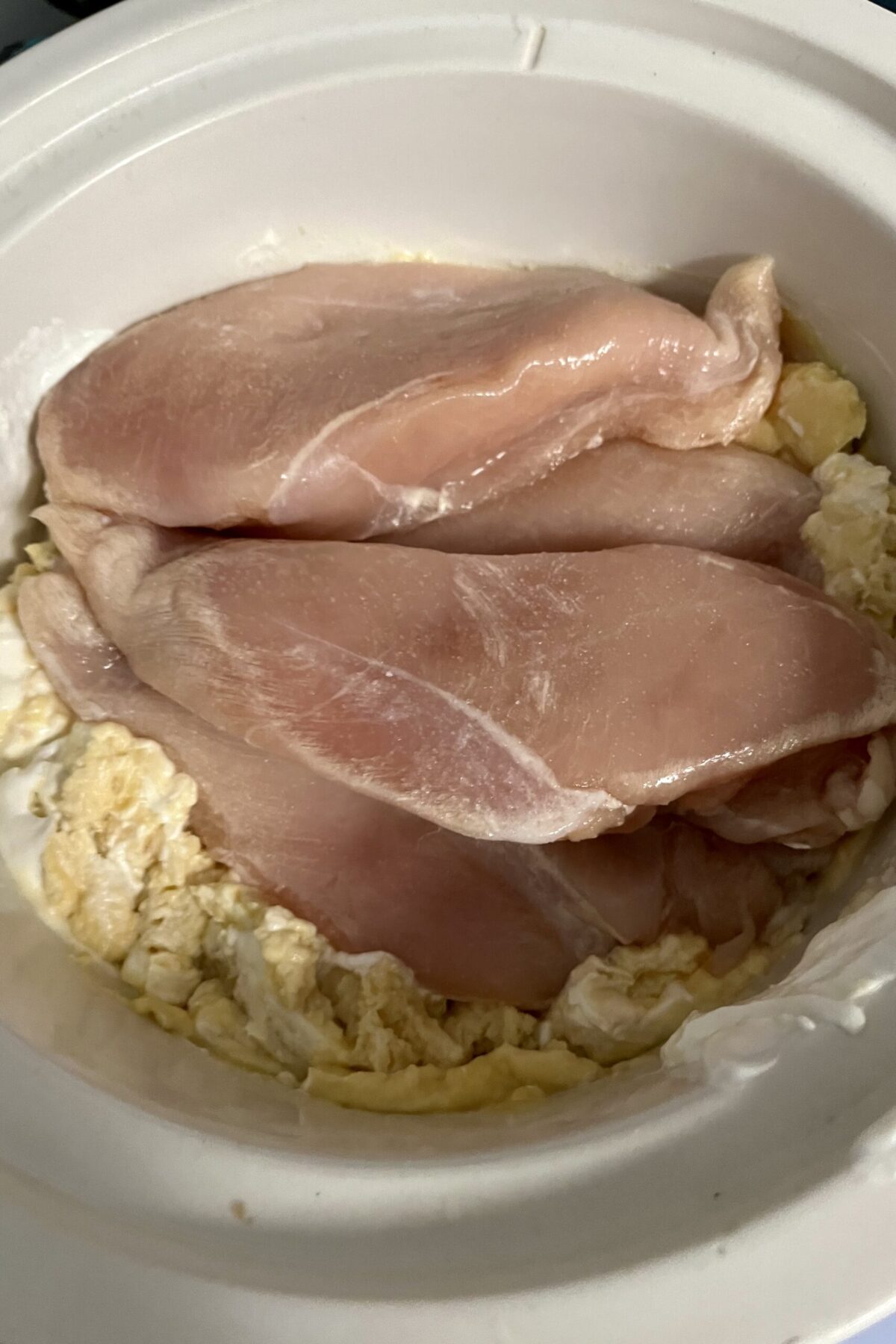 the slow cooker cheesy chicken is being started with cans, and the sour cream have been added into the slow cooker and I’ve been some more mixed. The chicken has also been added on top of. slow cooker the sauces kind of blond in the background, but the chicken really sticks out with pink