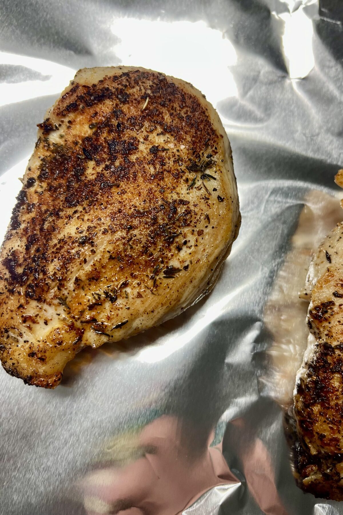 Seasoned chicken sitting on aluminum foil well has a nice brown color on it as well
