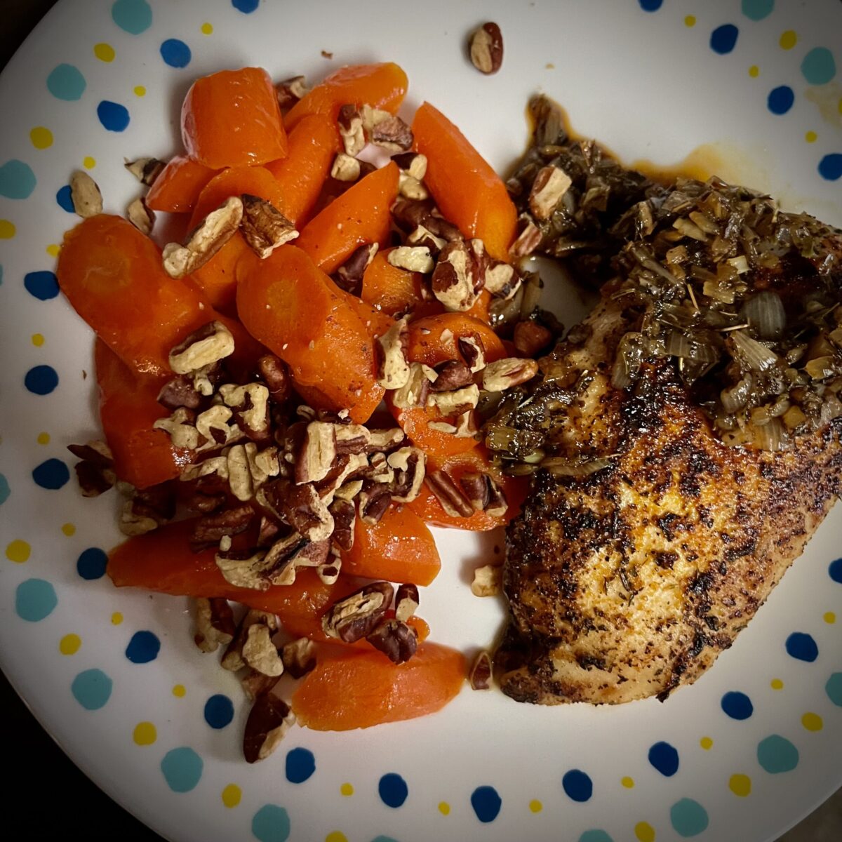 Pecans covering carrots on the right side of the plate have a nice shine to them chicken on the right side covered in seasoning and has nice sauce and shallots for a nice chicken Demi glaze with glazed carrots