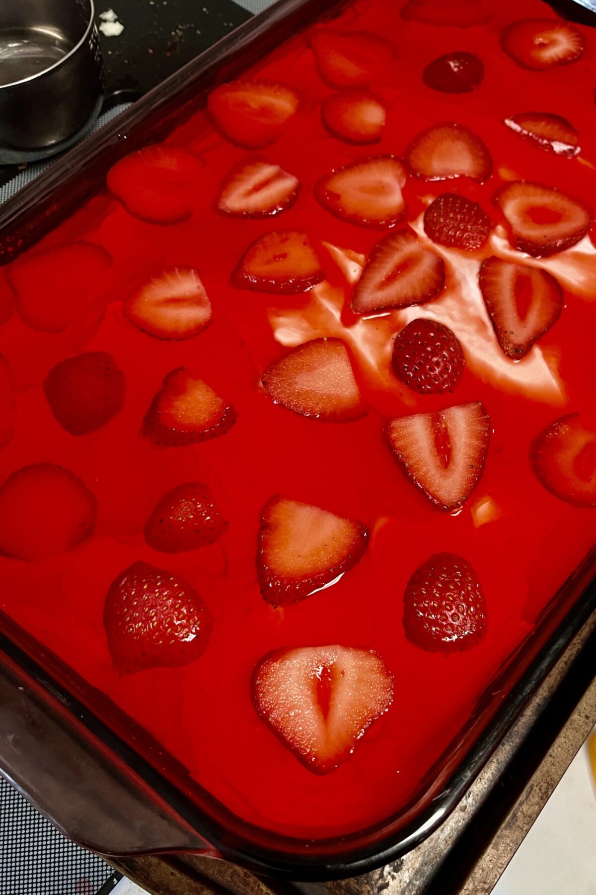 Strawberry pretzel salad is showing a little bit of cream cheese through the Jell-O because it did seep through the cream cheese layers from strawberries on top. There’s a little bit of a flower design in the middle.