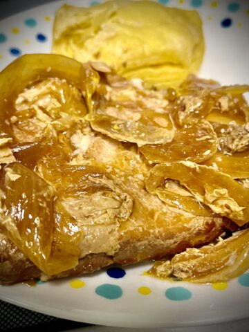 Pork chop on a plate covered with onions Sauce on it as well. There’s a biscuit sitting kind of a bright yellow color in the image.