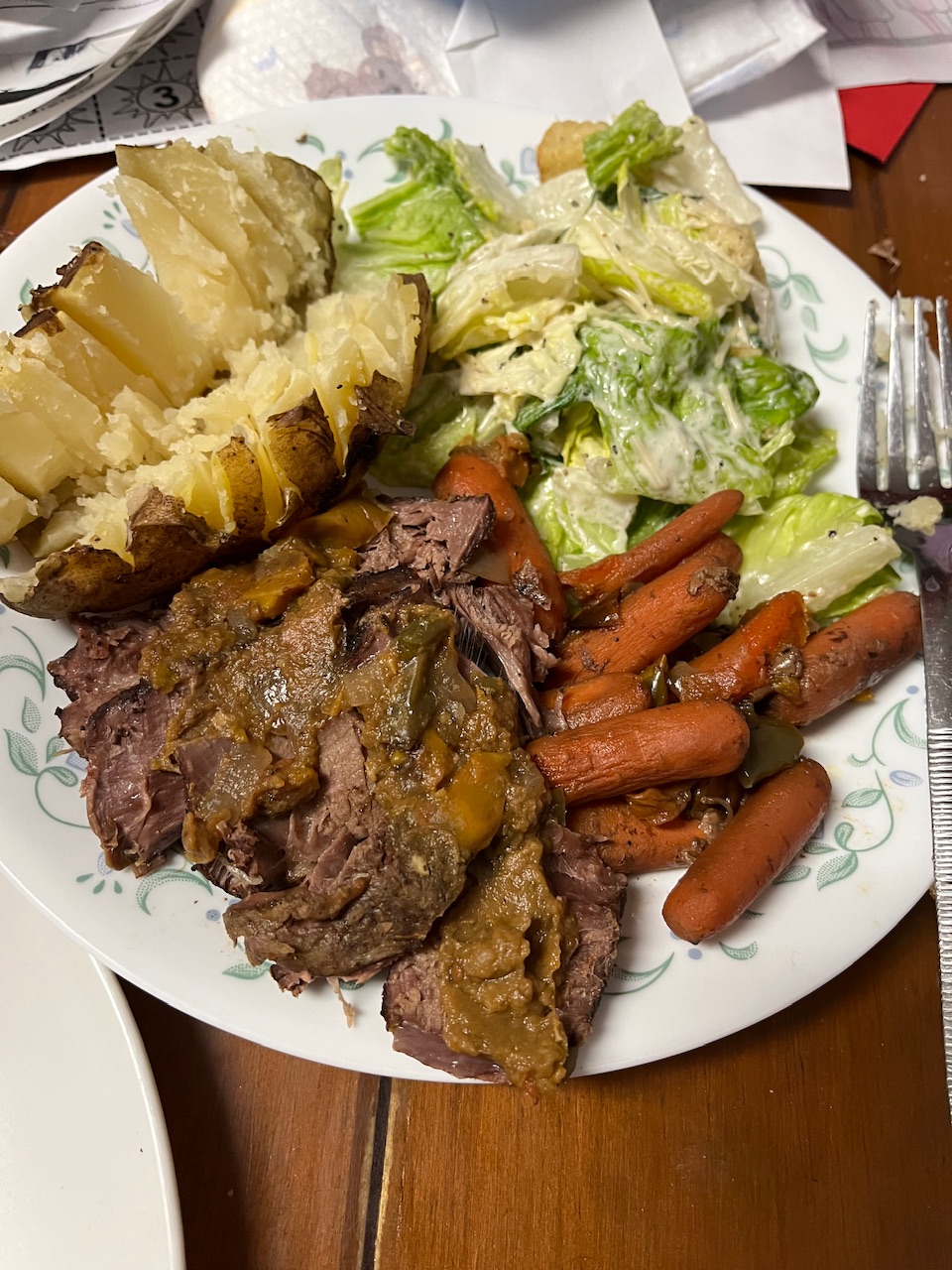 Play has been made up with some carrots roast potatoes potatoes has been sliced and a half as well with some salad sitting on a brown table