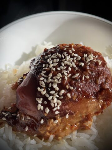 Square image showing part of a tumb and chicken on a bed of rice chicken is a dark red with some dead t9 brighten it up