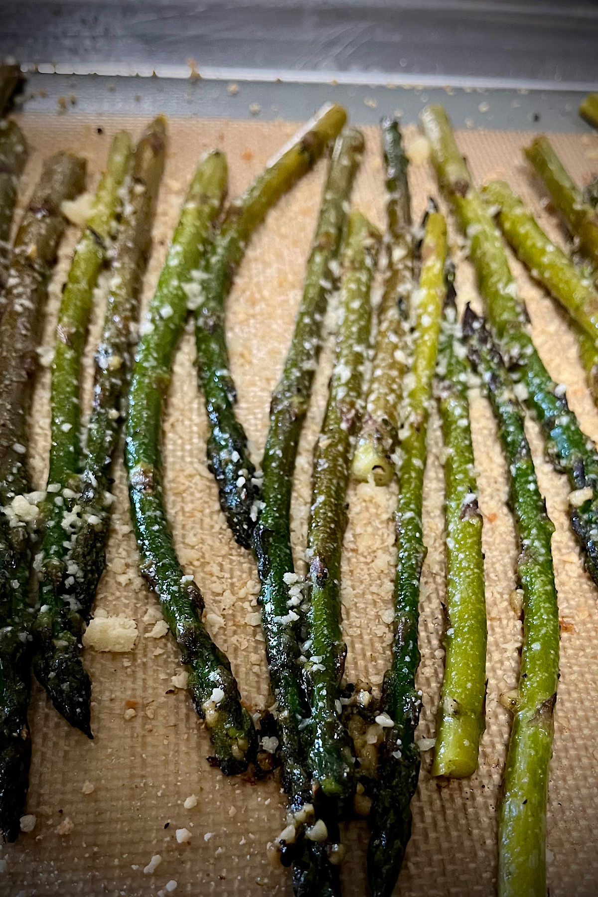 Easy roasted asparagus laying on a baking tray on a silicone mat contrast between the cheese and the dark green asparagus