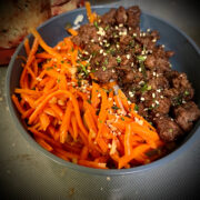 Square image of a Korean beef bowl I can see orange from the carrots, dark brown from the ground beef and the gray bowl sitting on top of the stove