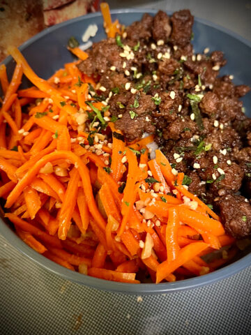 Square image of a Korean beef bowl I can see orange from the carrots, dark brown from the ground beef and the gray bowl sitting on top of the stove